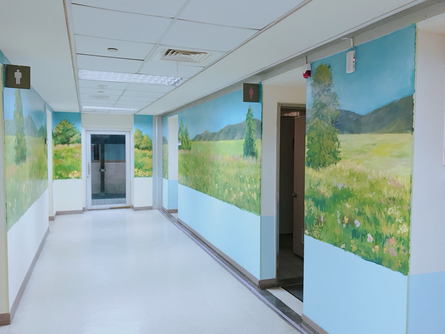 這張「醫院走廊」的照片是牆上畫著風景的圖案,走廊裡有通往另一個房間的門,還有一扇玻璃門,走廊的盡頭有一個廁所。